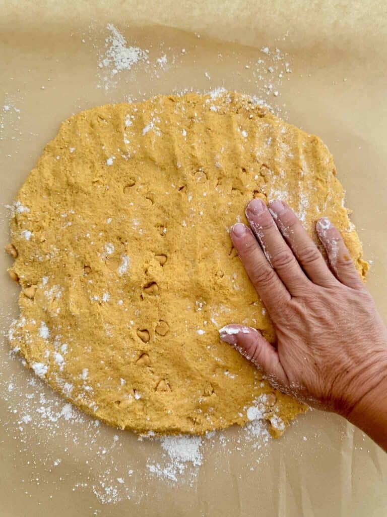 A hand shaping pumpkin scone dough into a round on a lightly floured surface.