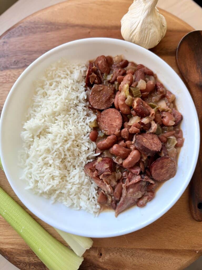 Savory Cajun red beans and sausage served with cooked white rice, lime, and garlic on a wooden tray. Perfect comfort food recipe for easy family dinners or meal prep.