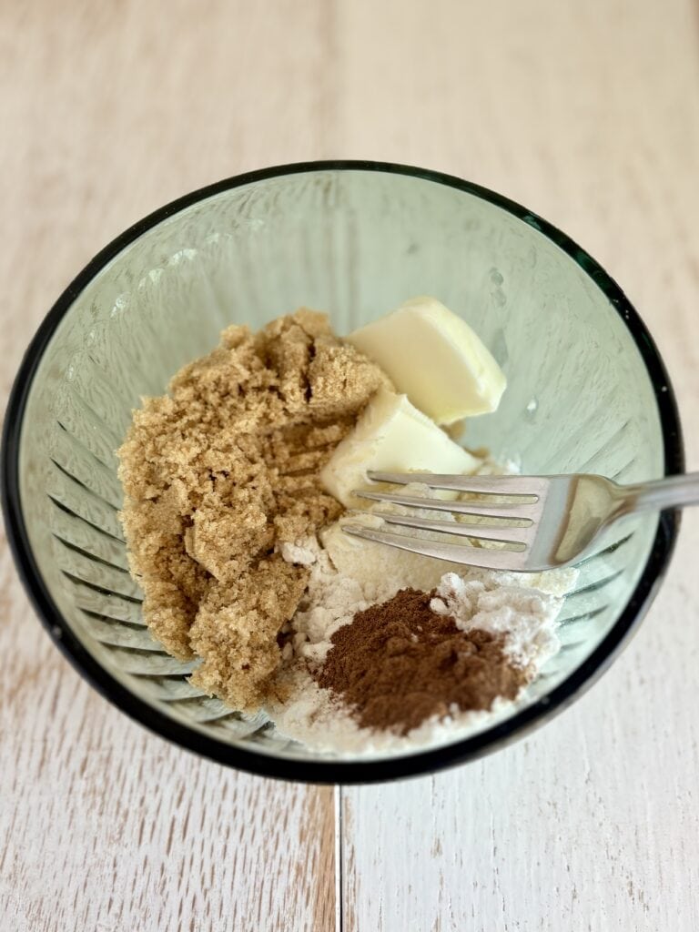 Streusel topping ingredients in a glass bowl, ready to be mixed, on a wooden surface.