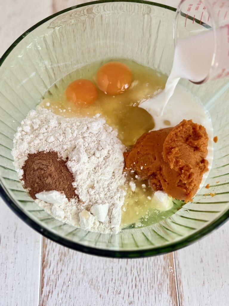 Eggs, flour, pumpkin puree, milk, and spices in a mixing bowl for baking pumpkin coffee cake. The ingredients are ready to be mixed for a delicious homemade pumpkin treat.