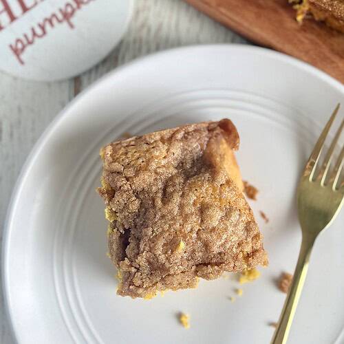 Golden brown pumpkin coffee cake with a crumbly topping, served on a white plate with a gold fork, perfect for fall comfort food recipes.