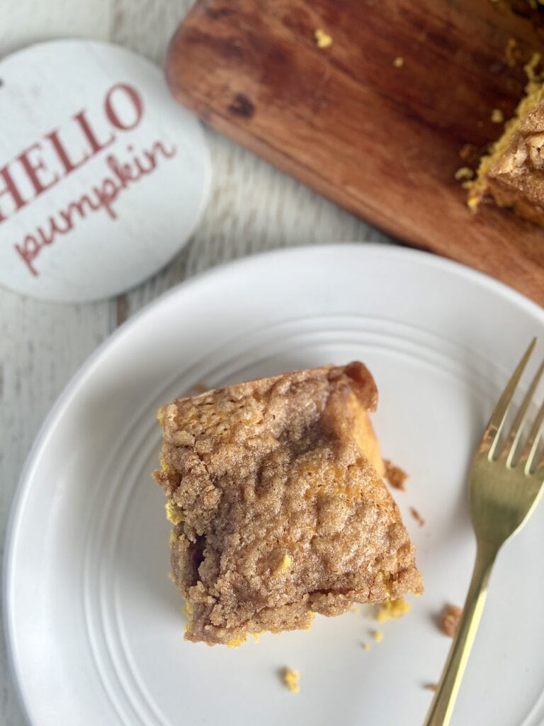 Golden brown pumpkin coffee cake with a crumbly topping, served on a white plate with a gold fork, perfect for fall comfort food recipes.