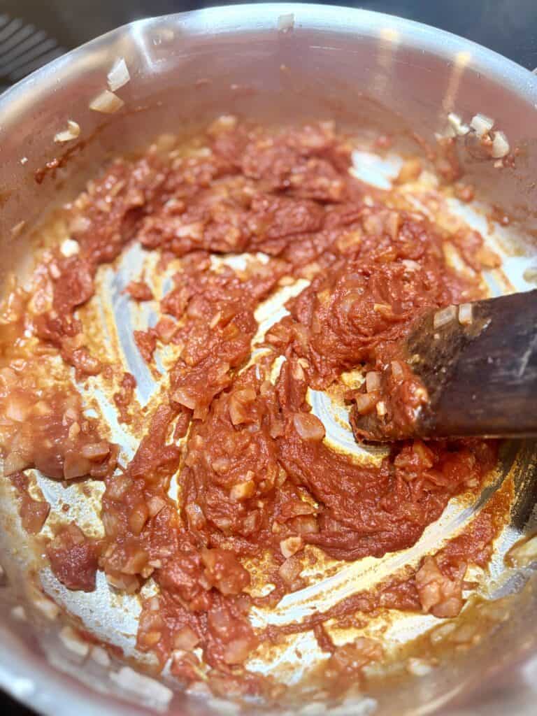 Rich tomato and onion sauce cooking in a stainless steel skillet, ideal for making flavorful pasta or Italian dishes. Perfect for hearty, homemade meals.