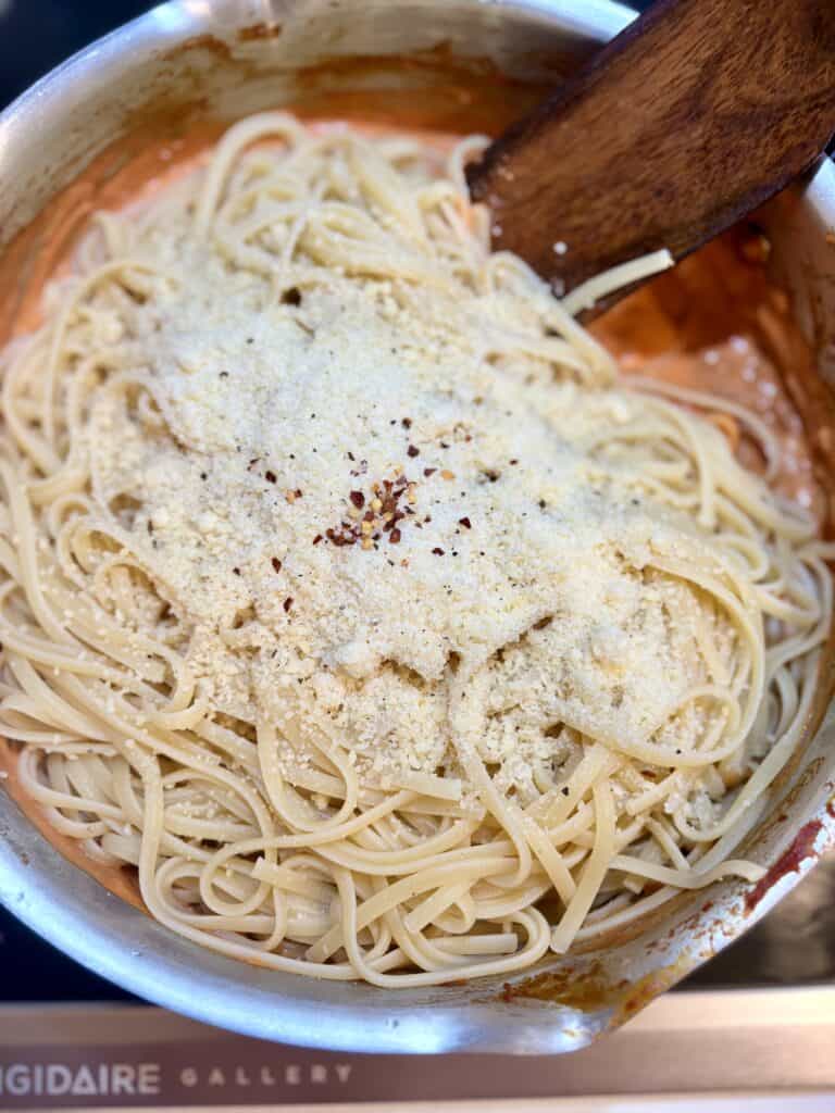 Creamy tomato spaghetti with grated cheese and red pepper flakes in a stainless steel skillet.