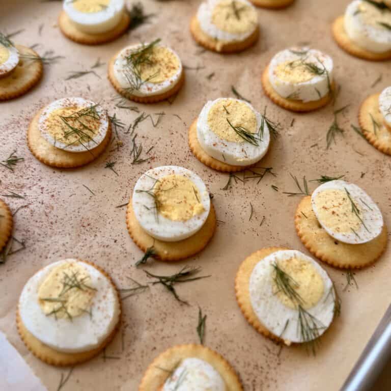 Deviled eggs garnished with fresh herbs on parchment paper, perfect for appetizer or party tray. Easy, delicious, and beautifully presented for gatherings or snack platters.