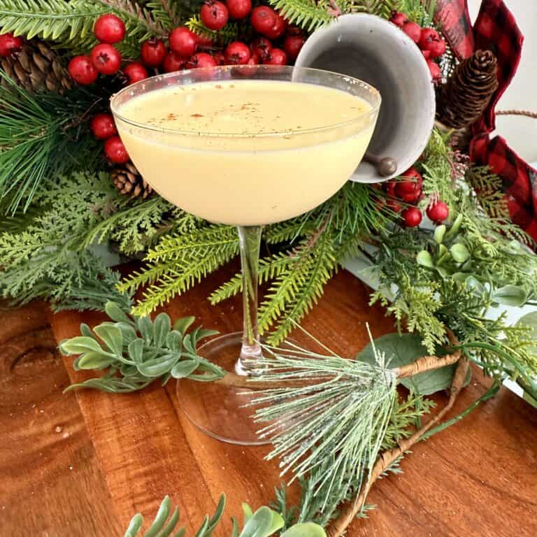 Frosted Christmas drink in a coupe glass on holiday-themed table with greenery and red berries, perfect for festive gatherings.