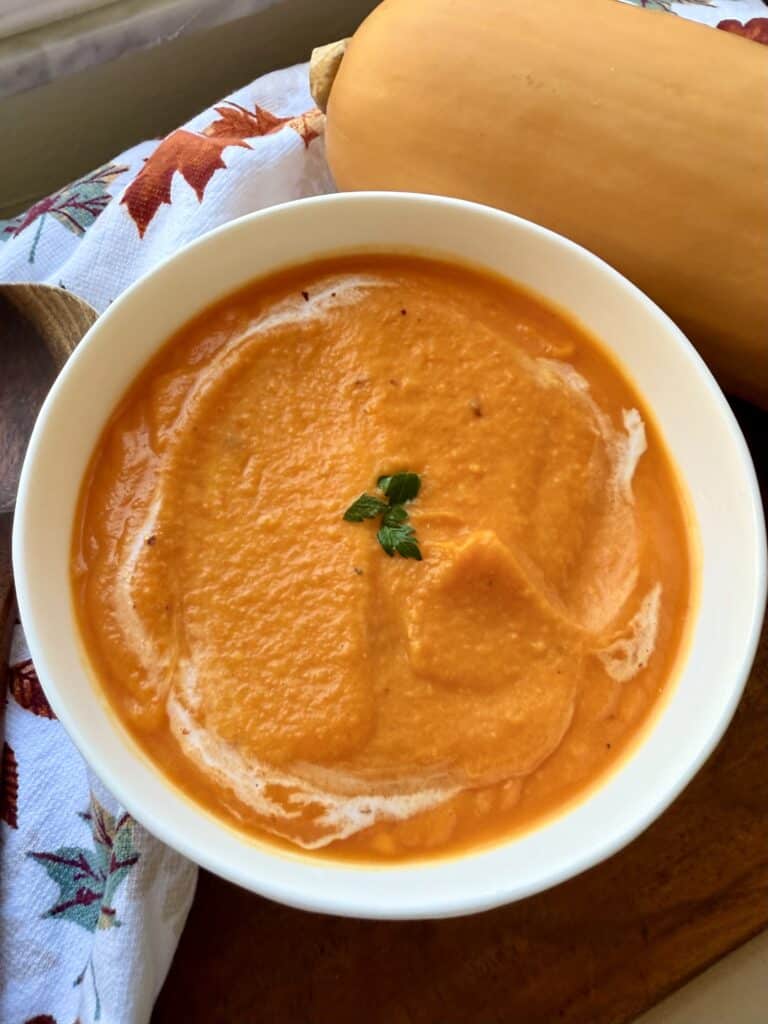 Creamy butternut squash soup with fresh herbs, served in a white bowl on a rustic wooden table, perfect for fall or winter meals.