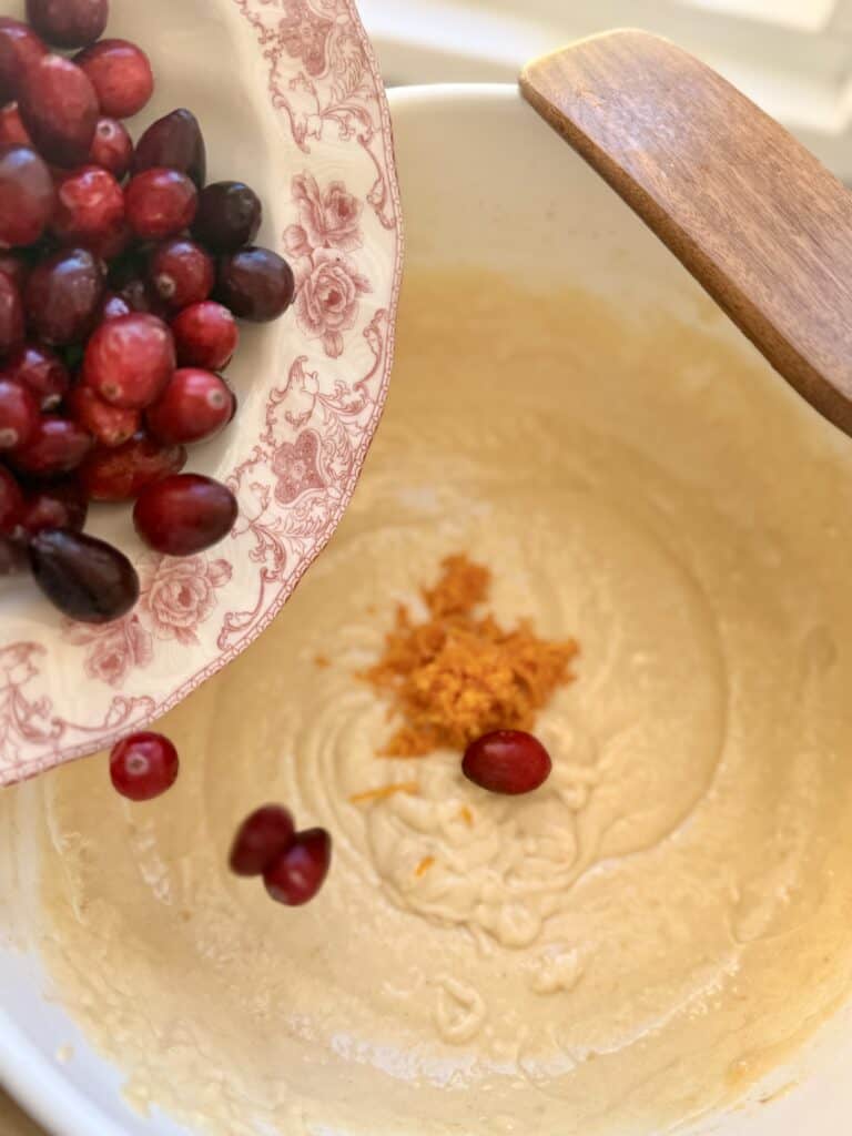 Fresh cranberries and orange zest being added to a batter in a mixing bowl for holiday baking.