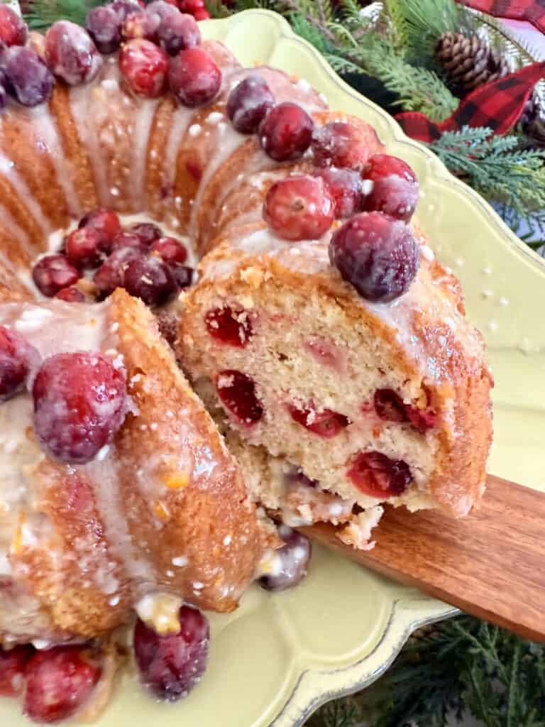 Fresh cranberry bread pudding with a glazed icing and topping of whole cranberries, served on a decorative green plate with holiday greenery in the background.