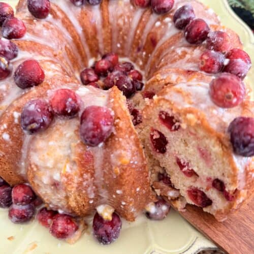Fresh cranberry coffee cake with icing, topped with whole cranberries, on a decorative plate, ideal for holiday gatherings, featuring a moist crumb and vibrant seasonal fruit.