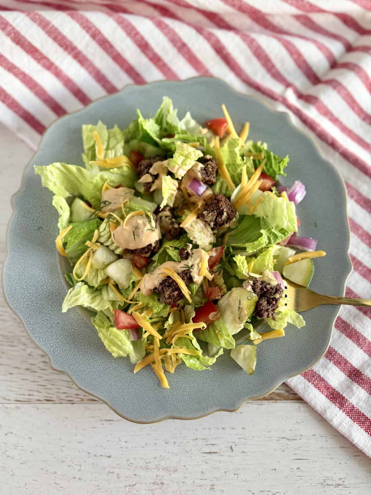 Fresh homemade Big Mac salad with seasoned ground beef, crisp lettuce, shredded cheese, tomatoes, onions, and creamy dressing, served on a stylish blue plate for a quick, healthy meal.