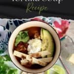 Delicious chicken tortilla soup in a bowl with avocado, cheese, cilantro, and crispy tortilla strips, served with lime wedges. Perfect for a comforting and flavorful meal.