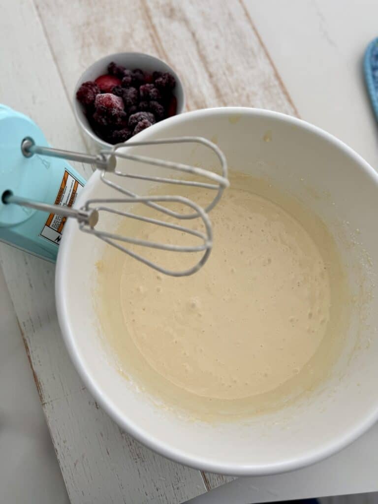 Delicious berry bundt cake batter prepared in a large mixing bowl, ready to be baked. The image showcases fresh berries, a hand mixer, and baking ingredients, perfect for a sweet dessert recipe.