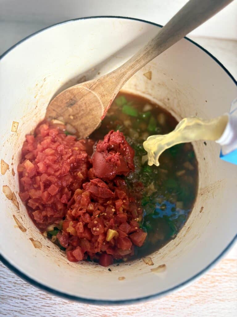 Chopped tomatoes, onions, peppers and herbs cooking in a white pot 