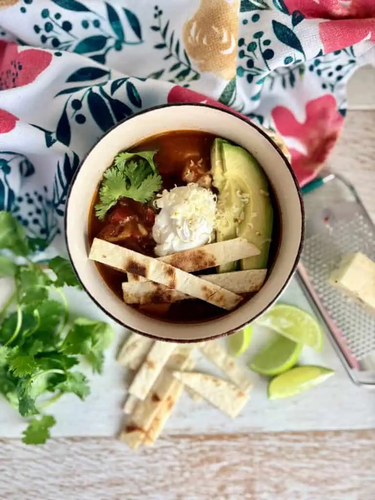Healthy chicken tortilla soup with avocado, lime, and cilantro in a bowl.