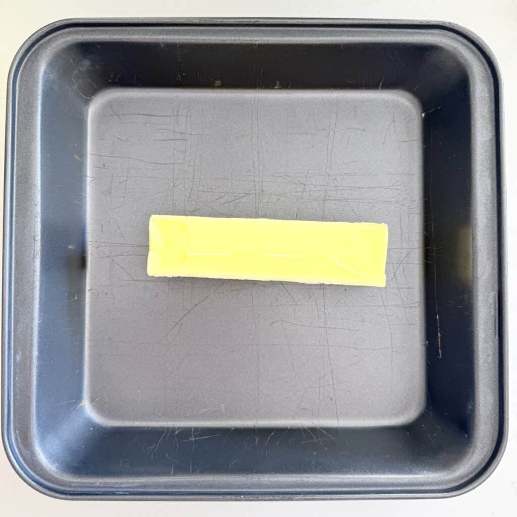 Unsalted butter un melted in an 8 x 8 baking pan on the counter.