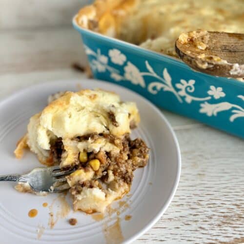 Classic beef shepherd's pie with mashed potatoes, served in a blue floral dish, featuring a slice on a white plate with a fork, perfect comfort food.