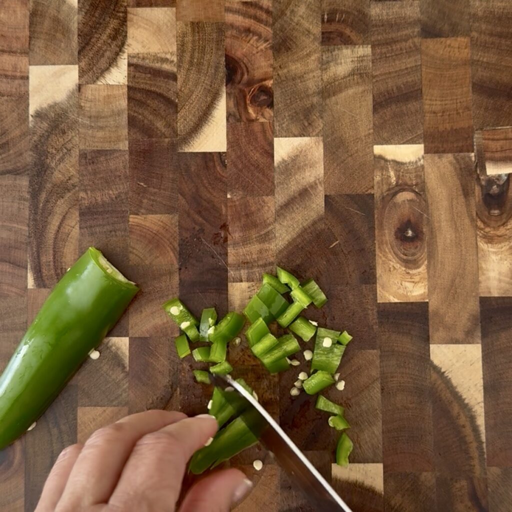Using sharp knife on a cutting board to dice jalapeño pieces