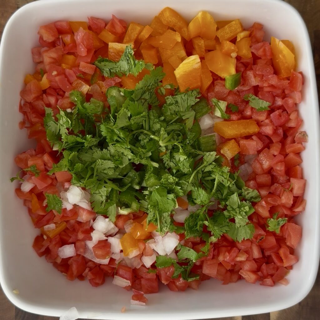 This vibrant pico de gallo features a colorful mix of chopped tomatoes, onions, jalapeños, and cilantro, offering a fresh and zesty flavor. Ideal for enhancing Mexican dishes or serving as a healthy snack, this homemade salsa is a staple in Mexican cuisine. The image showcases a bowl of freshly prepared pico de gallo, emphasizing its bright colors and fresh ingredients, perfect for adding a burst of flavor to any meal.