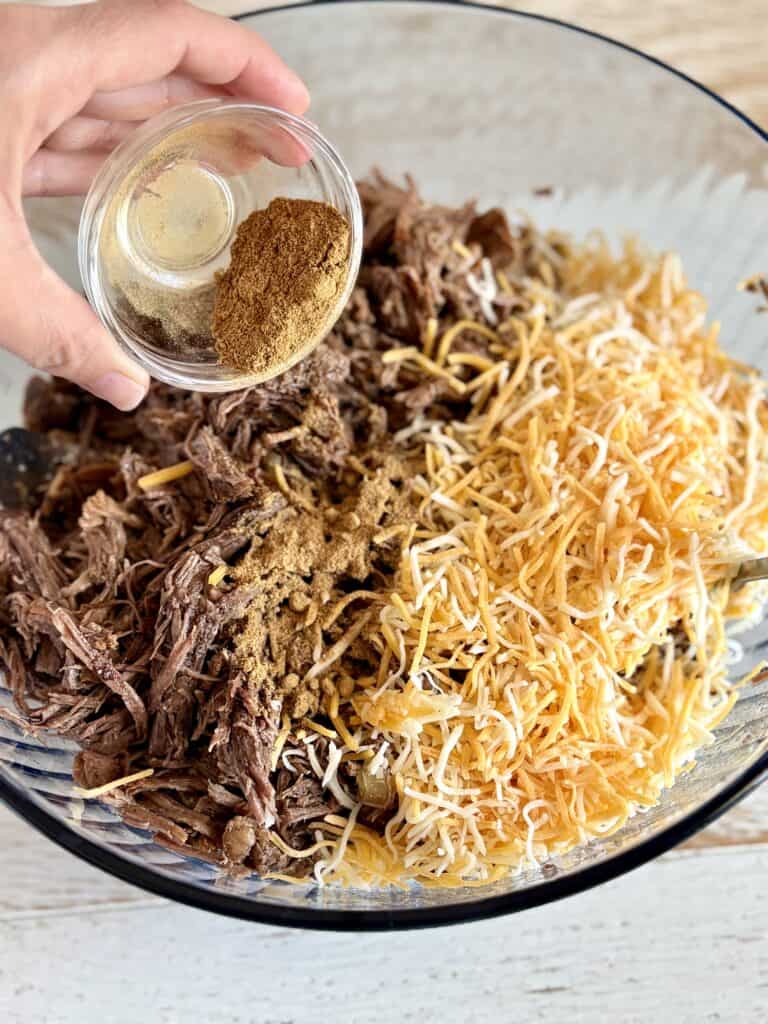 Juicy shredded beef with shredded cheddar cheese in a glass bowl, ready to be served as delicious nachos, seasoned with spices for a flavorful meal.
