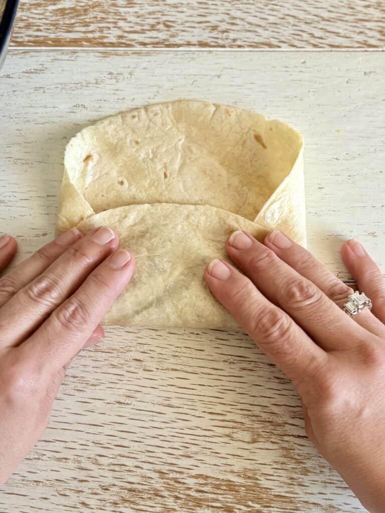 tortilla being folded by hands on a wooden surface. Perfect for making tacos, wraps, or burritos with authentic flavor and soft texture.