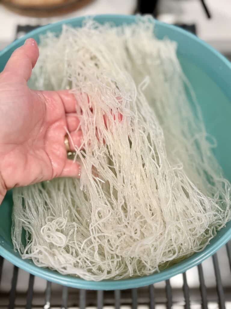 A hand holding rice stick over a bowl of water