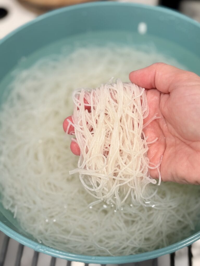 a hand holding softened rice stick over a bowl of water