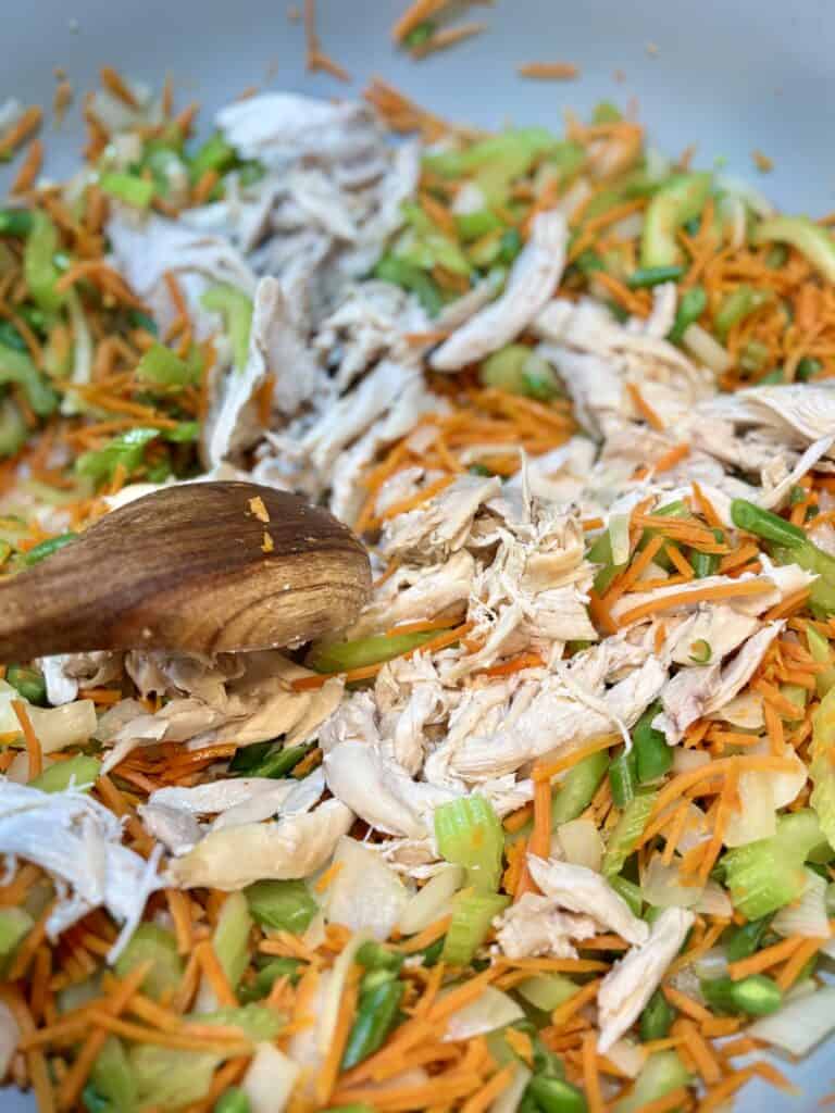 Cooked shredded chicken mixed with colorful vegetables like carrots, celery, and green onions in a skillet, ready for serving or further cooking.