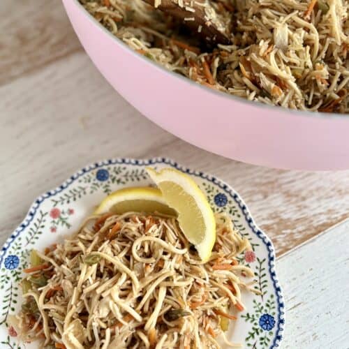 Pancit served in a pink bowl, garnished with lemon wedges, featuring shredded chicken, noodles, and vegetables. Perfect for quick, flavorful meals.