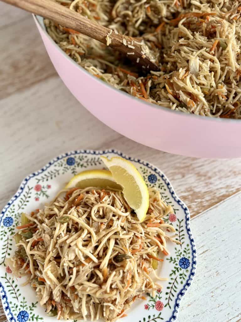 Pancit served in a pink bowl, garnished with lemon wedges, featuring shredded chicken, noodles, and vegetables. Perfect for quick, flavorful meals.