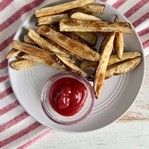 Crispy homemade French fries served with a side of ketchup on a white plate, perfect for snack or side dish.