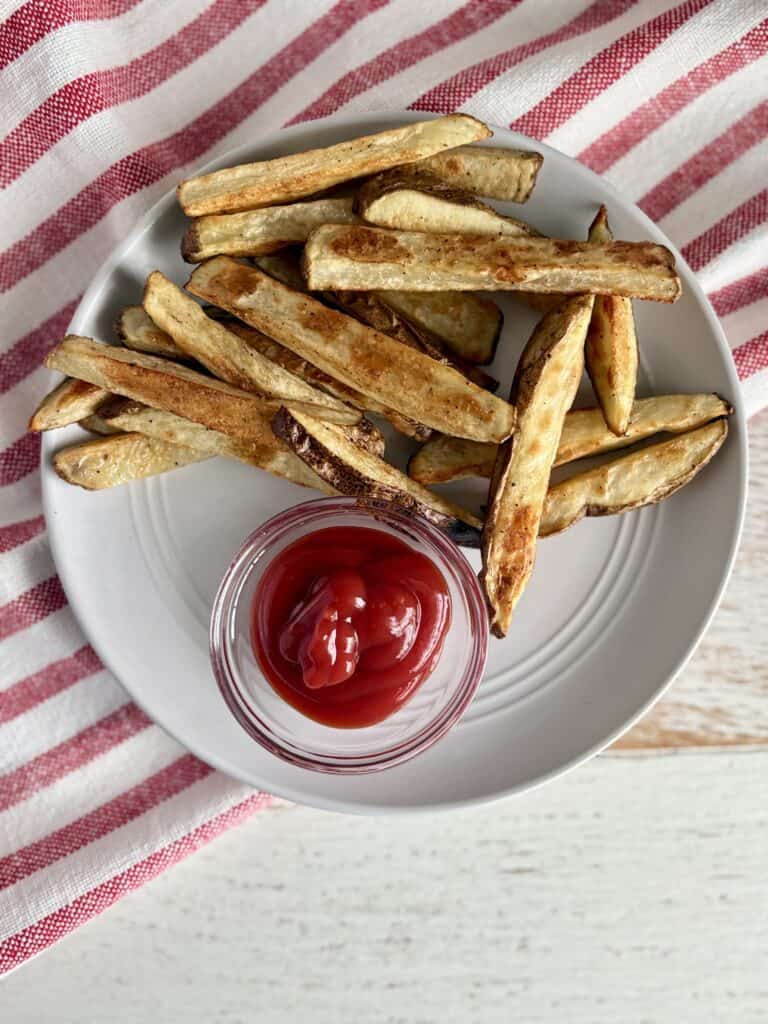 Crispy homemade French fries served with a side of ketchup on a white plate, perfect for snack or side dish.