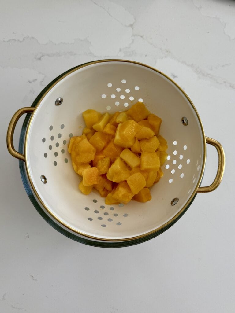 Draining excess liquid from thawed mangoes in a colander
