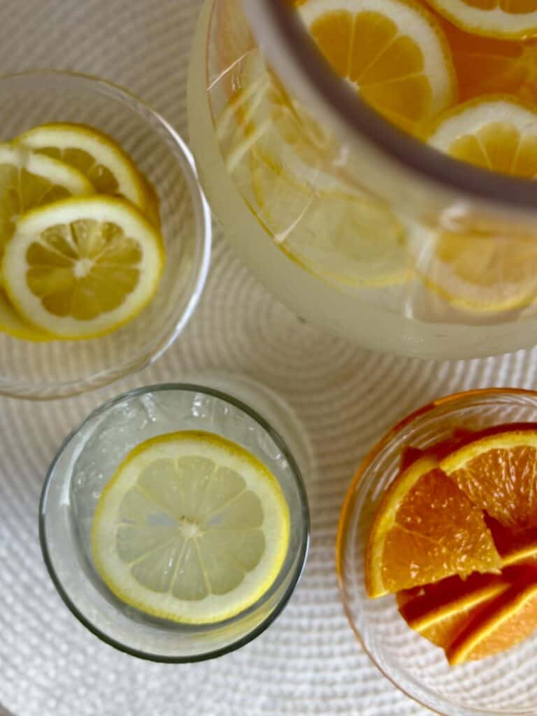 Refreshing citrus vodka lemonade pitcher with lemon and orange slices in glasses.
