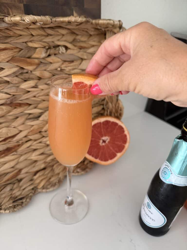 Refreshing grapefruit mimosa in a champagne flute, garnished with a slice of grapefruit, on a white surface with a woven basket in the background.