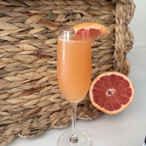 Glass of fresh grapefruit cocktail garnished with a grapefruit slice, placed in front of a woven basket, showcasing a vibrant, citrusy drink perfect for summer.