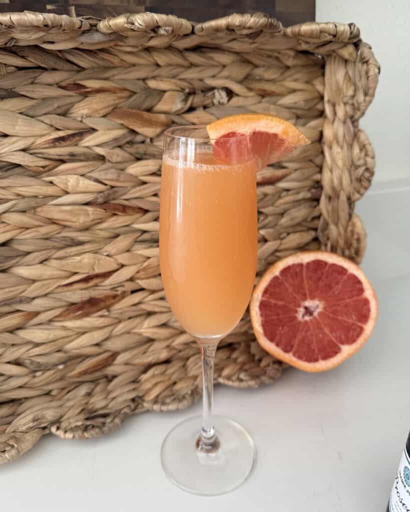 Glass of fresh grapefruit cocktail garnished with a grapefruit slice, placed in front of a woven basket, showcasing a vibrant, citrusy drink perfect for summer.