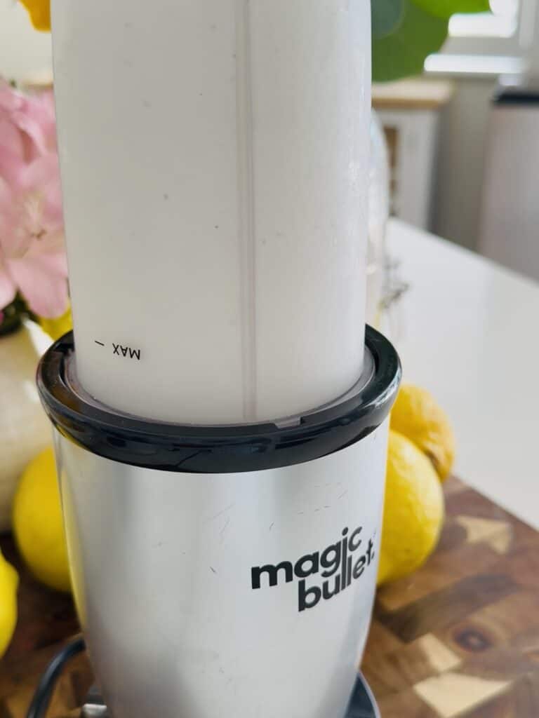Magic Bullet blender with a creamy lemon mixture, fresh lemons in the background, on a wooden countertop, perfect for making whipped frozen lemonade.