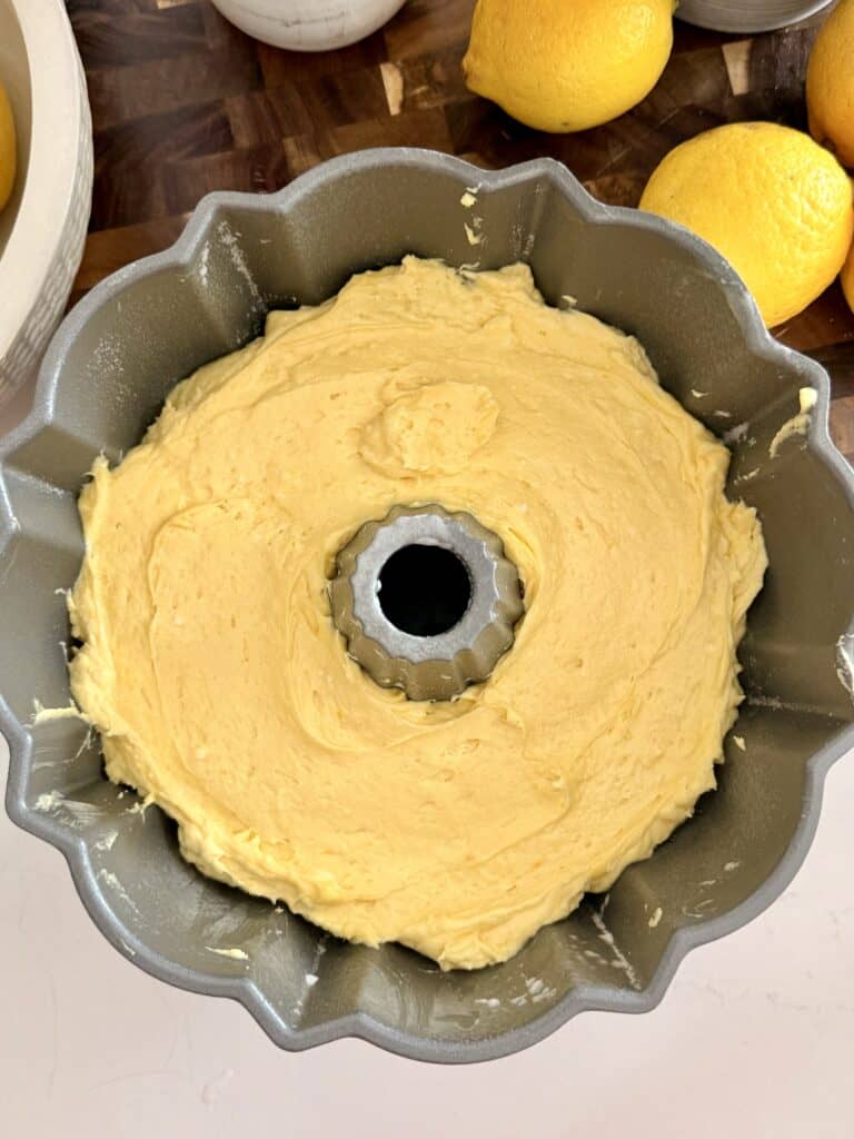 Lemon cake batter for the poundcake is in the prepared and greased Bundt canton on the counter.