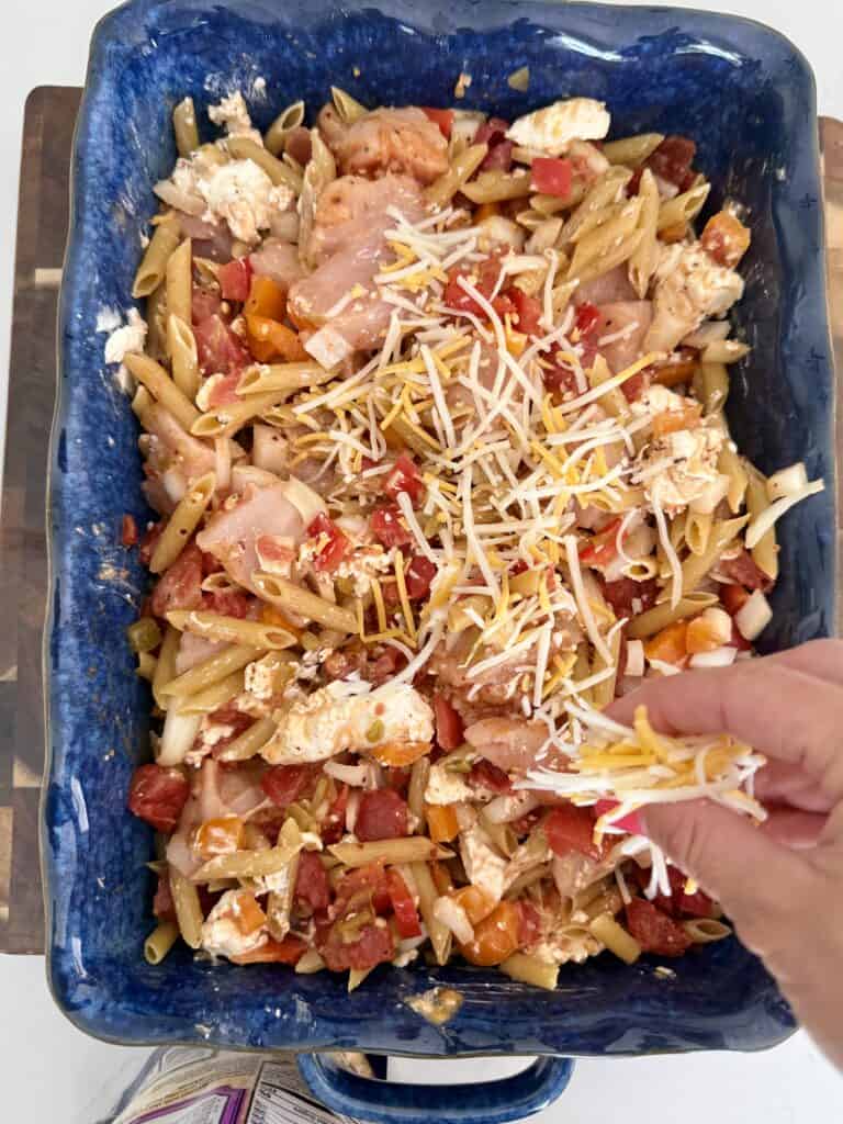 Close-up of Chicken Fajita Penne Pasta in a blue baking dish with shredded cheese and colorful vegetables.