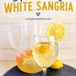Sparkling white sangria in a glass next to a pitcher of sangria on a blue placemat