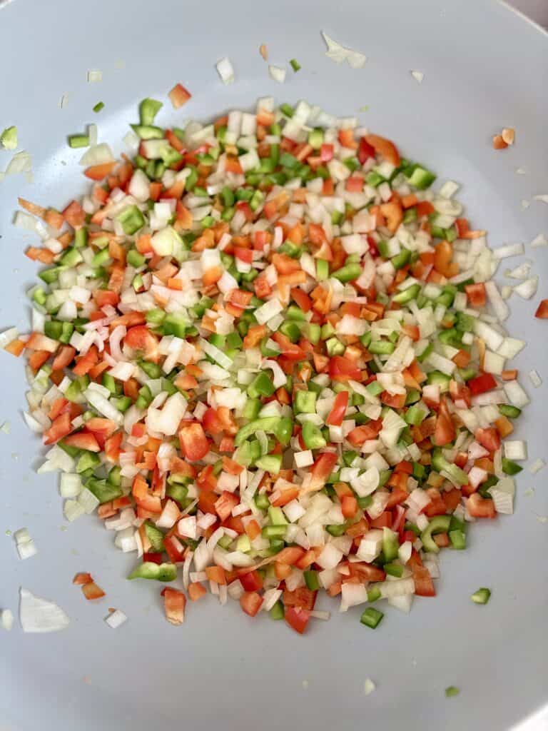 Colorful chopped vegetables including onions, bell peppers, and celery in a gray pan, ready for cooking or recipe preparation.