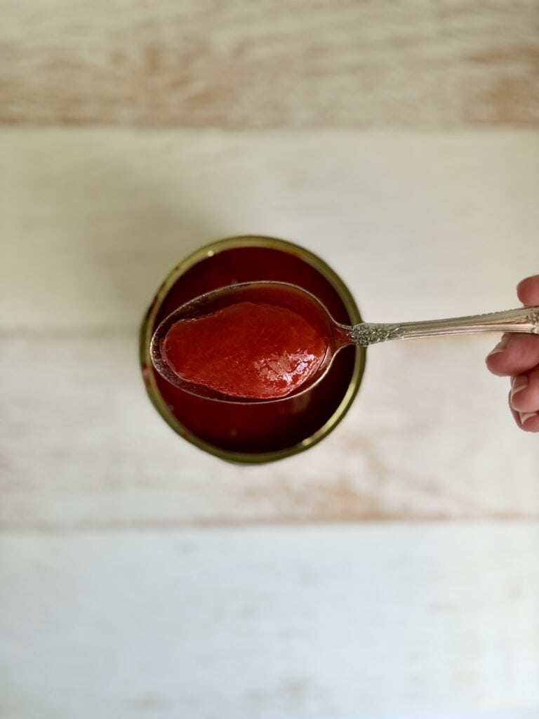 A canned whole tomato being lifted from a can with a slotted spoon