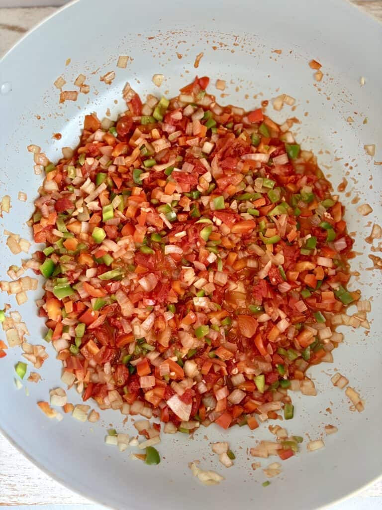 Colorful mixture of diced tomatoes, onions, and green peppers being cooked in a large skillet
