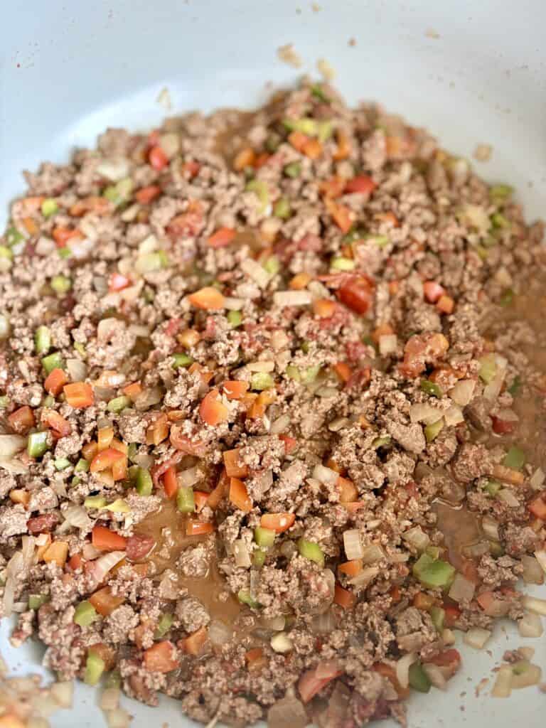 Ground beef cooked with diced peppers, tomatoes, and onions in a large skillet.