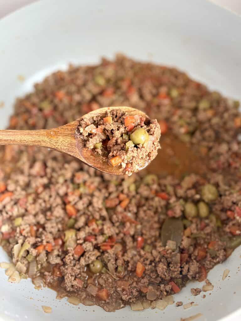 Close-up of cooked ground beef with tomatoes, peppers, onions, and spices in a large skillet.