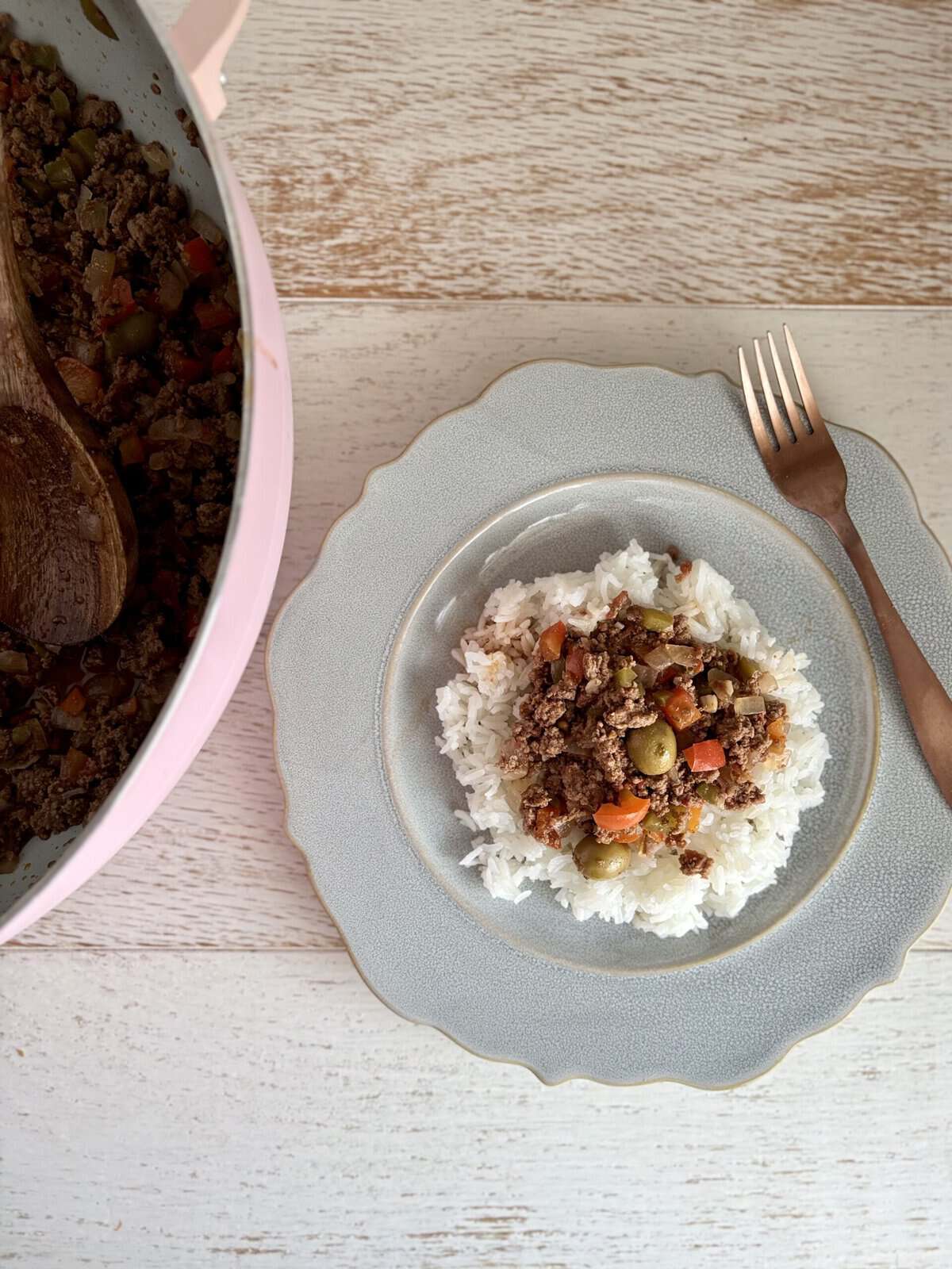 A plate of homemade beef picadillo served over rice, with a fork on the side, on a light wooden table.