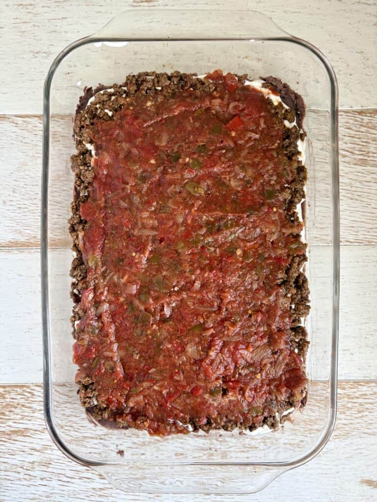 Baked taco dip casserole with tomato salsa in a glass dish, ready to bake, from Simply Made Dish.