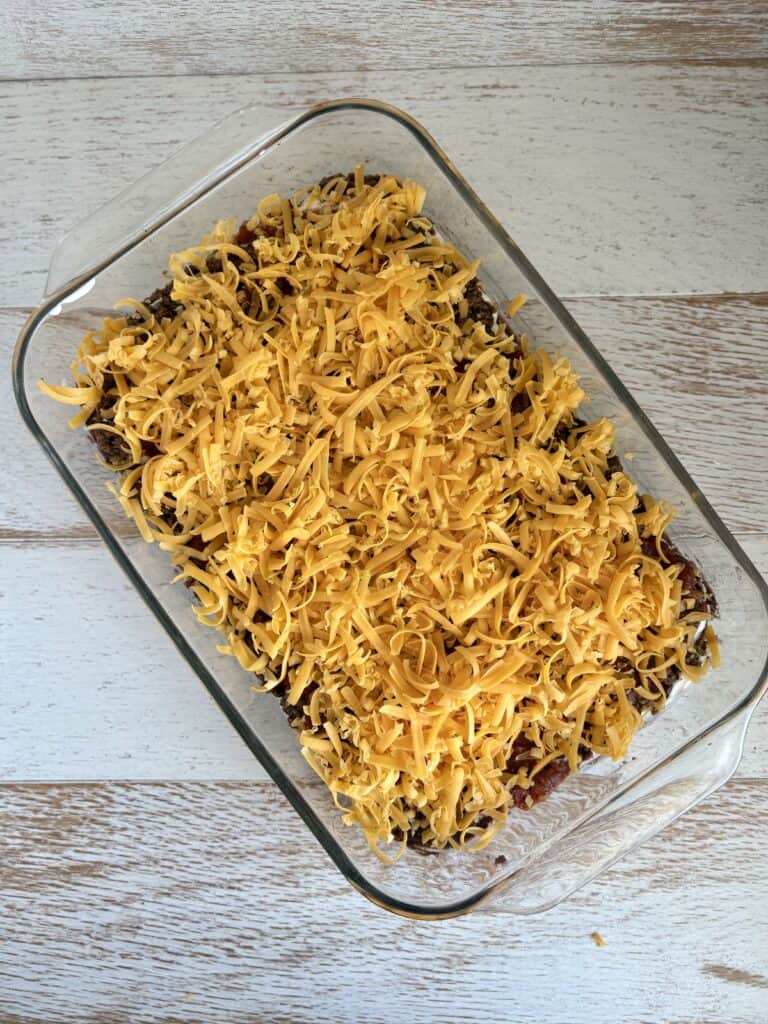 Cheese sprinkled over the top of a layered taco dip ready for the oven