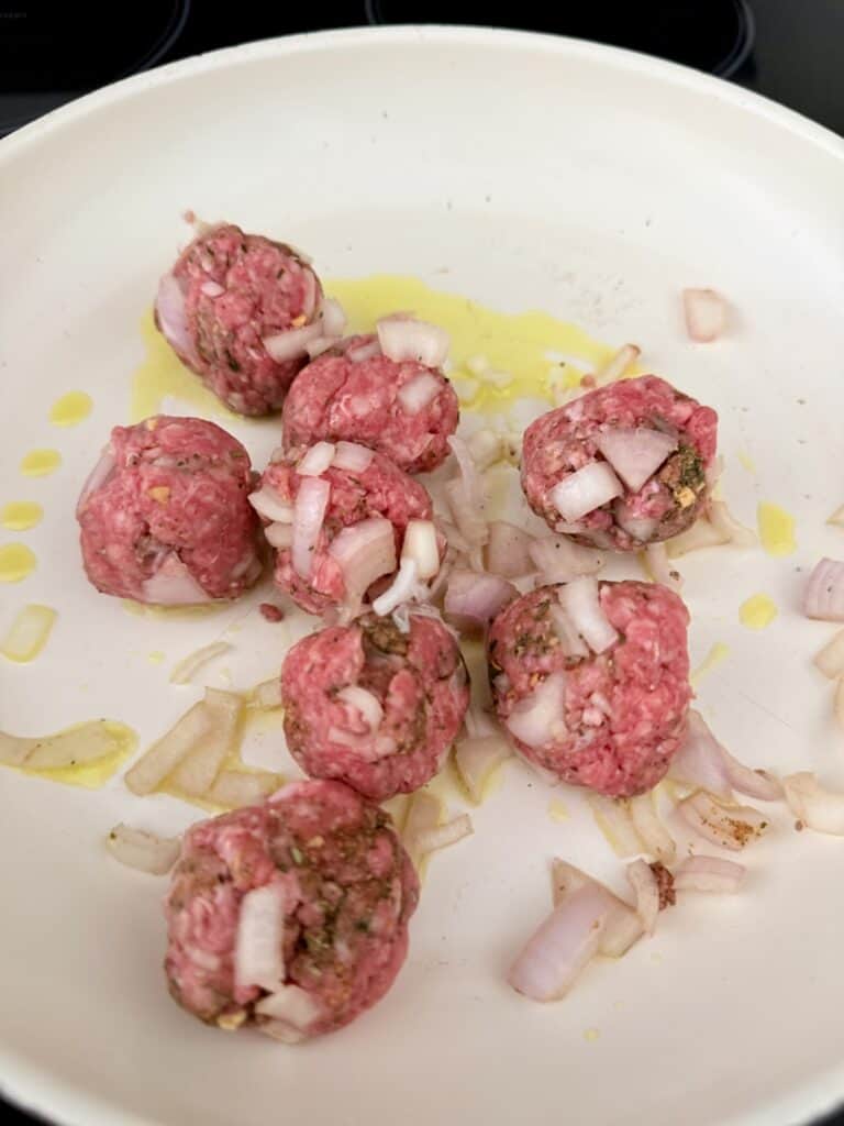 meatballs with herbs and diced shallots in a frying pan on the stove top.